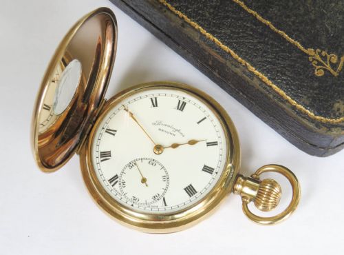 fig 1. A gold-plated half hunter pocket watch displayed open, featuring a white enamel dial with black Roman numerals and a subsidiary seconds dial.