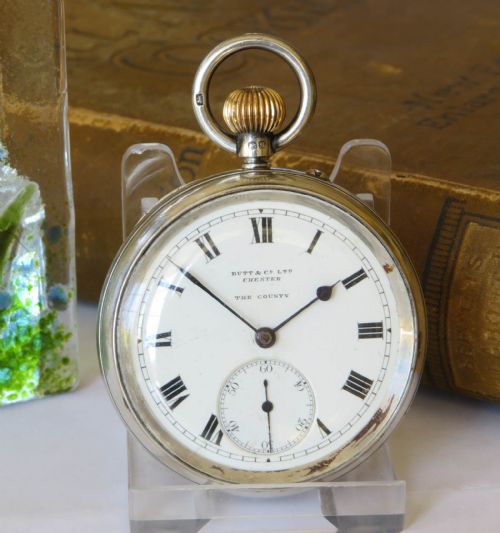 fig 1. An open-face antique silver pocket watch featuring a white enamel dial with black Roman numerals and a subsidiary seconds sub-dial.