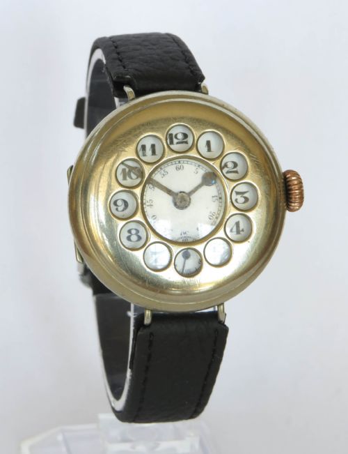 fig 1. A military trench watch featuring a polished metal shrapnel guard with circular hour cutouts over a white enamel dial with a black leather strap.