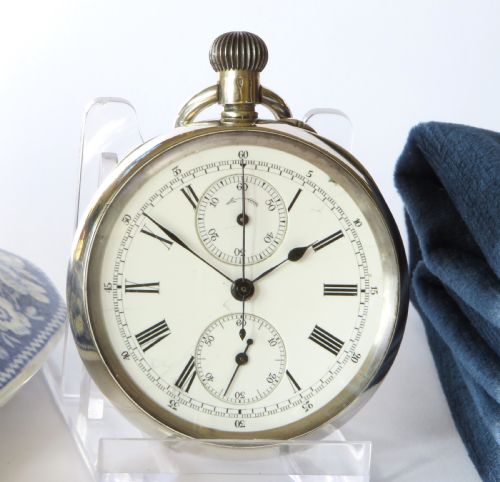 fig 1. An antique open-faced silver chronograph pocket watch featuring a white enamel dial with Roman numerals and dual sub-dials.