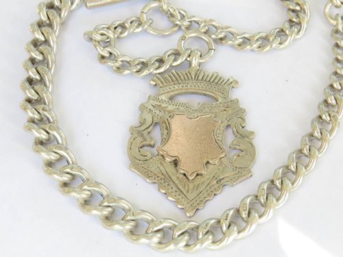 fig 1. An antique sterling silver Albert watch chain with curb links, a T-bar, swivel clasp, and an engraved shield fob featuring rose gold detail.