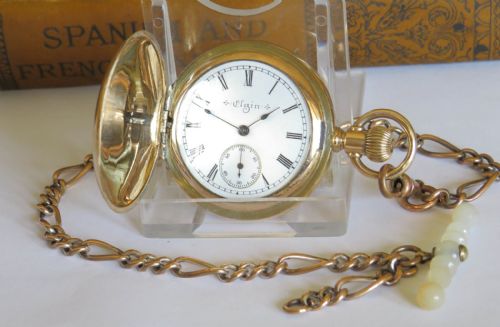 fig 1. A gold-coloured full hunter pocket watch featuring an engraved monogram on the casing, attached to a matching link chain with a decorative toggle.