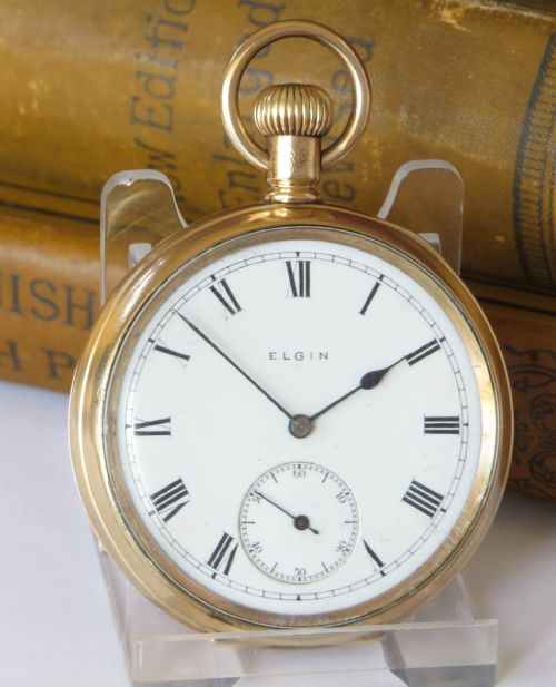 fig 1. An antique gold-coloured open-face Elgin pocket watch featuring a white enamel dial with black Roman numerals and a small seconds sub-dial.