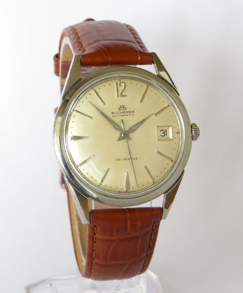 fig 1. A vintage gentlemens Bucherer automatic wrist watch featuring a champagne dial with baton indices, date window, silver-toned metal case, and textured brown leather strap.