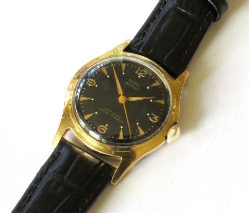 fig 1. A 1950s gents Berg Parat wristwatch featuring a gold-plated case, a black dial with gold numerals, and a black leather strap.
