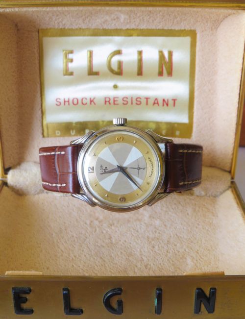 fig 1. A 1950s Elgin Shockmaster wrist watch with a two-tone dial and brown leather strap, displayed alongside its original brass presentation box and papers.
