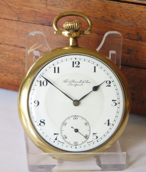 fig 1. A 1930s gold-tone open-face pocket watch featuring a white enamel dial, black Arabic numerals, a sub-seconds dial at six oclock, and signature marked Thomas Russell and Son Liverpool.