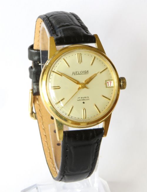 fig 1. A 1950s gents Heloisa wrist watch with a circular gold-tone case, cream dial with gold baton markers, date aperture at three oclock, and black leather strap.