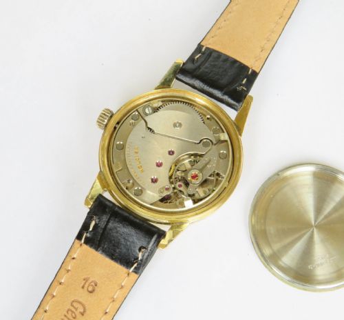 fig 2. A 1950s gents Heloisa wrist watch with a circular gold-tone case, cream dial with gold baton markers, date aperture at three oclock, and black leather strap.