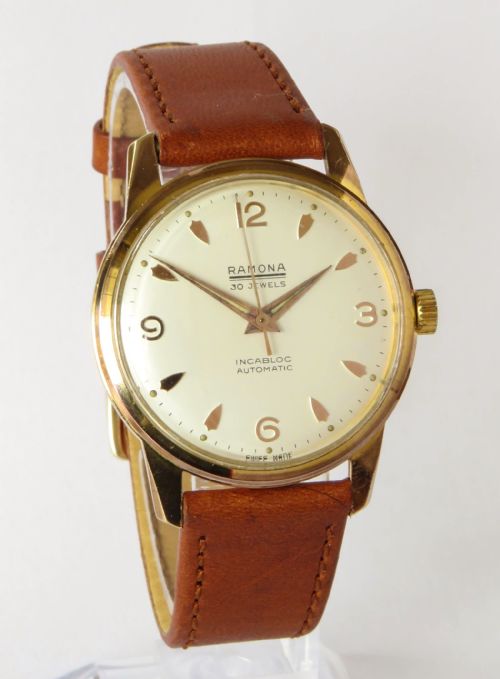 fig 1. A 1950s gentlemens Ramona automatic wristwatch featuring a gold-plated case, cream dial with arrow-shaped markers, and a stitched tan leather strap.