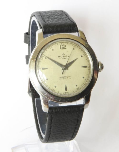 fig 1. A 1950s gents wristwatch featuring a round stainless steel case, an off-white dial with silver-tone hour markers, and a black textured leather strap.