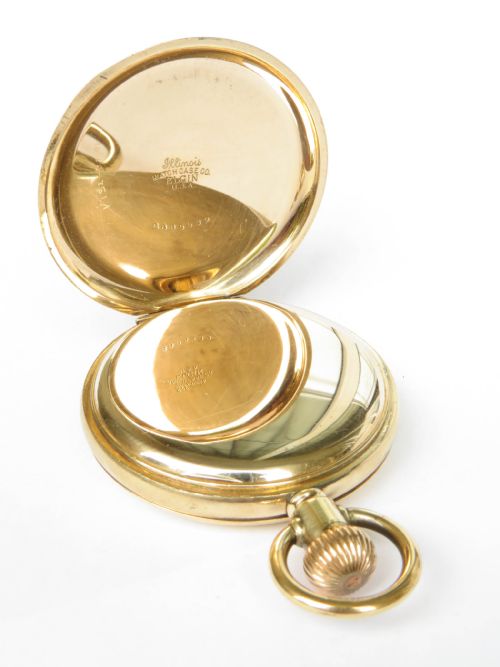 fig 2. An opened gold-toned half hunter pocket watch featuring a white enamel dial, black Roman numerals, and a sub-seconds dial.