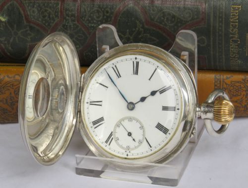 fig 1. An English sterling silver half hunter pocket watch featuring blue enamel Roman numerals around a central glass aperture.