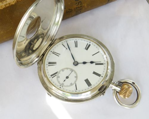 fig 2. An English sterling silver half hunter pocket watch featuring blue enamel Roman numerals around a central glass aperture.