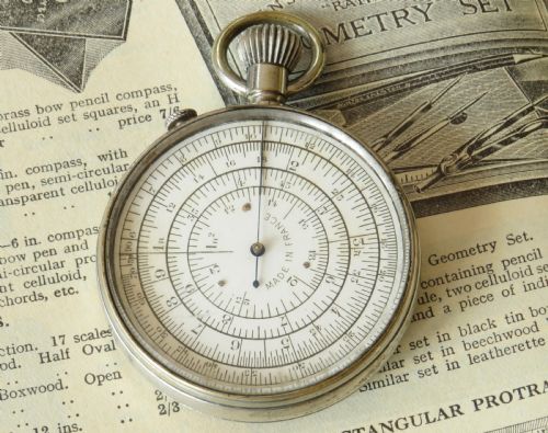 fig 1. A pocket watch styled mechanical circular slide rule with a nickel case, white dial featuring concentric scales, and text reading Calculigraphe H.C. Paris.