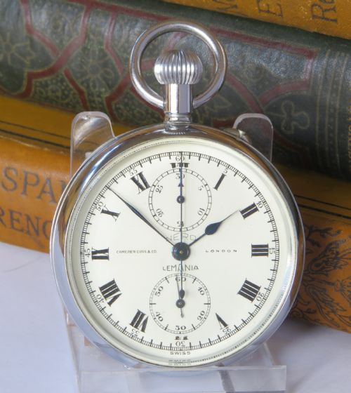 fig 1. A 1930s open-face chronograph pocket watch featuring a white dial with Roman numerals, two subsidiary dials, and a chrome-plated metal case.