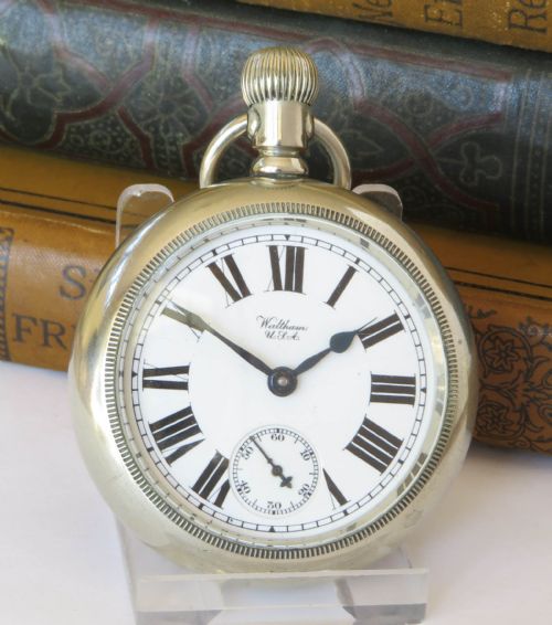 fig 1. An antique silver-tone open-face pocket watch featuring a white enamel dial with black Roman numerals and a subsidiary seconds dial.