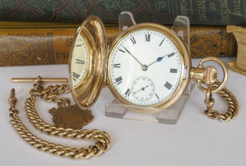fig 1. An antique gold-coloured full hunter pocket watch open to reveal a white dial with Roman numerals, alongside a curb link chain and decorative shield fob.