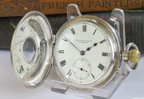 fig 1. An antique silver half-hunter pocket watch featuring an outer case with blue Roman numerals and a central dial marked Hamilton and Inches Edinburgh.