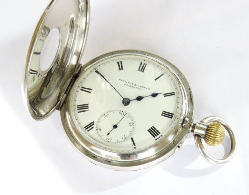 fig 2. An antique silver half-hunter pocket watch featuring an outer case with blue Roman numerals and a central dial marked Hamilton and Inches Edinburgh.