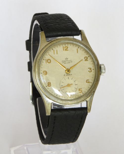 fig 1. A 1950s Smiths De Luxe gents wristwatch featuring a textured cream dial with gold-tone Arabic numerals, sub-seconds dial, and a black leather strap.