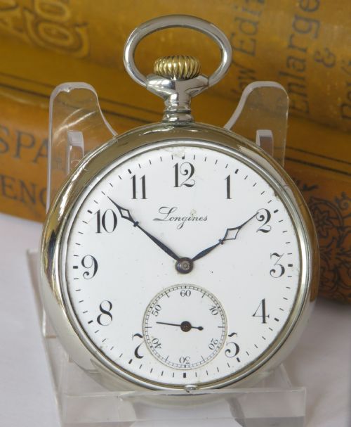 fig 1. An antique open face Longines pocket watch featuring a white enamel dial with black Arabic numerals, a sub-seconds dial, and a silver casing with a brass crown.