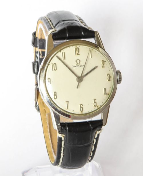 fig 1. A 1963 mens Omega wrist watch featuring a round stainless steel case, a cream dial with Arabic numerals, and a black leather strap with white stitching.