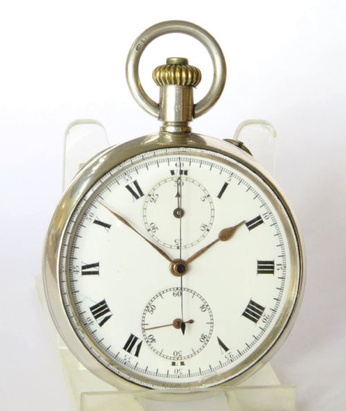 fig 2. An open-face antique silver chronograph pocket watch featuring a white enamel dial with black Roman numerals, two subsidiary dials, and a gold-toned winding crown.