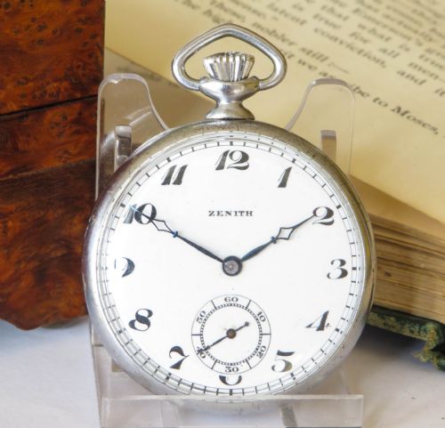 fig 1. An open-face 1930s Zenith pocket watch featuring a white enamel dial with black Art Deco Arabic numerals, subsidiary seconds dial, and silver-toned metal case.