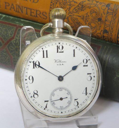 fig 1. An open-face antique silver pocket watch featuring a white enamel dial, black Arabic numerals, and a subsidiary seconds dial at six oclock.