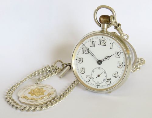 fig 1. An open-face silver pocket watch with a white enamel dial, black numerals, and sub-seconds dial, attached to a silver curb-link chain with a military badge fob.