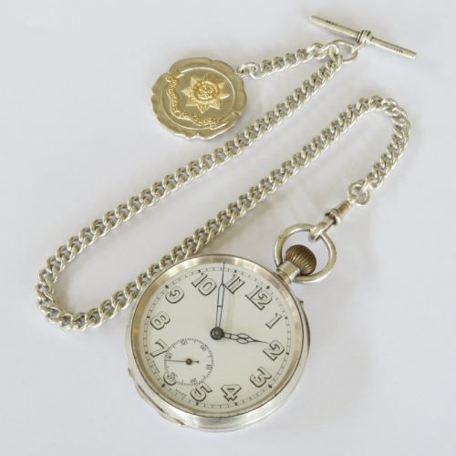 fig 2. An open-face silver pocket watch with a white enamel dial, black numerals, and sub-seconds dial, attached to a silver curb-link chain with a military badge fob.