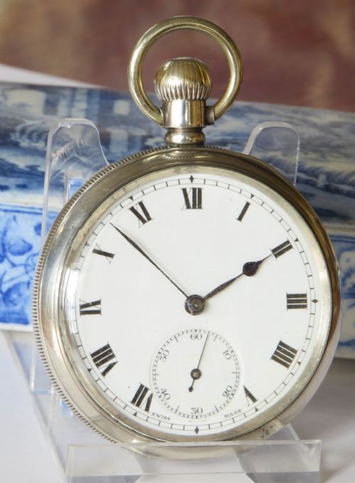 fig 1. An antique open-face silver pocket watch displaying a white enamel dial with black Roman numerals and a small seconds sub-dial at six oclock.