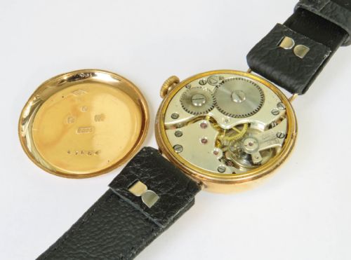 fig 2. An antique 9ct gold trench watch featuring a white enamel dial with black numerals, a red twelve, fixed wire lugs, and a black leather strap.