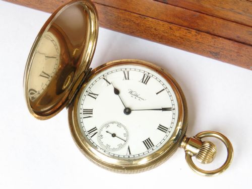 fig 1. An open antique gold-toned Waltham full hunter pocket watch displaying a white enamel dial with black Roman numerals and a subsidiary seconds dial.