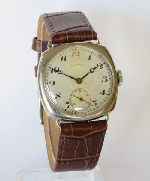fig 1. A 1930s cushion-shaped stainless steel wristwatch featuring a light dial with black Arabic numerals, a red twelve marker, a subsidiary seconds dial, and a textured brown leather strap.