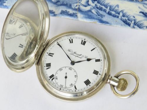 fig 1. An open antique silver full hunter pocket watch displaying a white enamel dial with black Roman numerals and a subsidiary seconds dial.