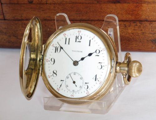 fig 1. A gold-toned Waltham half hunter pocket watch with Roman numerals engraved around the central circular dial aperture.