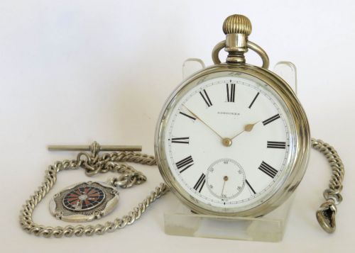 fig 1. An antique open-face Longines pocket watch with a white enamel Roman numeral dial, connected to a silver-coloured curb chain with an enamelled fob medallion.