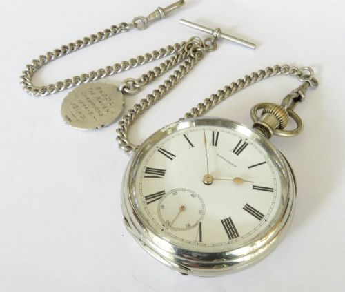 fig 2. An antique open-face Longines pocket watch with a white enamel Roman numeral dial, connected to a silver-coloured curb chain with an enamelled fob medallion.