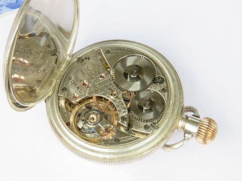fig 3. An open-face antique silver pocket watch featuring a white enamel dial with black Arabic numerals, a sub-seconds dial, and a ribbed gold-toned crown.