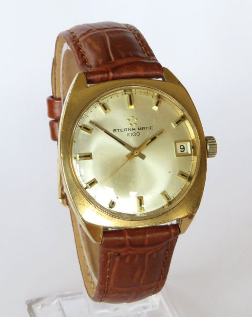 fig 1. A 1969 gents Eterna-Matic 1000 wristwatch featuring a gold-toned cushion case, champagne dial with date aperture, and brown leather strap.