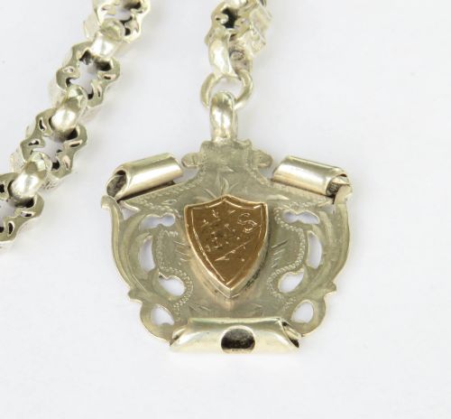 fig 1. An antique sterling silver pocket watch chain featuring decorative carved links, a T-bar attachment, a swivel clasp, and a shield-shaped fob with gold detailing.