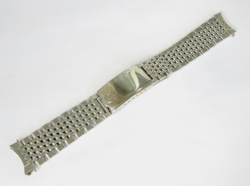 An overhead view of a segmented stainless steel Omega watch bracelet with a branded clasp against a neutral background.