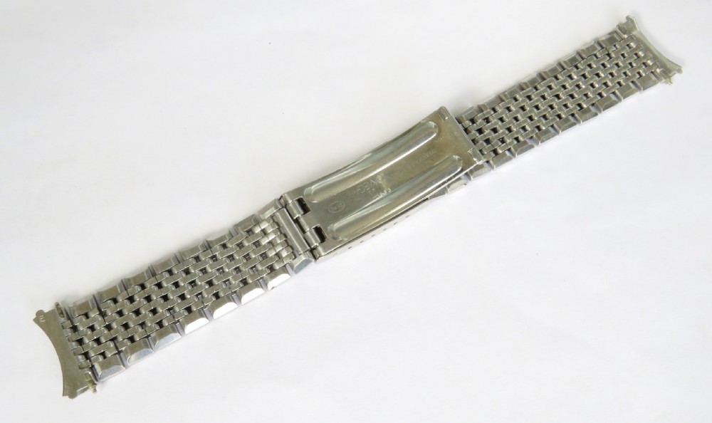 An overhead view of a segmented stainless steel Omega watch bracelet with a branded clasp against a neutral background. View II