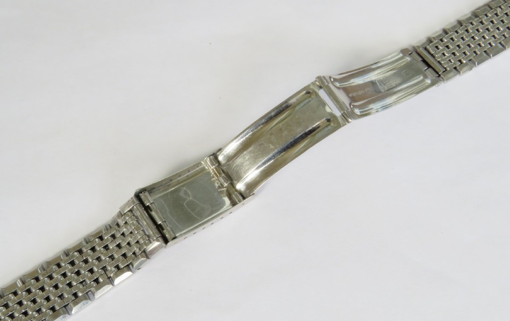 An overhead view of a segmented stainless steel Omega watch bracelet with a branded clasp against a neutral background. View III
