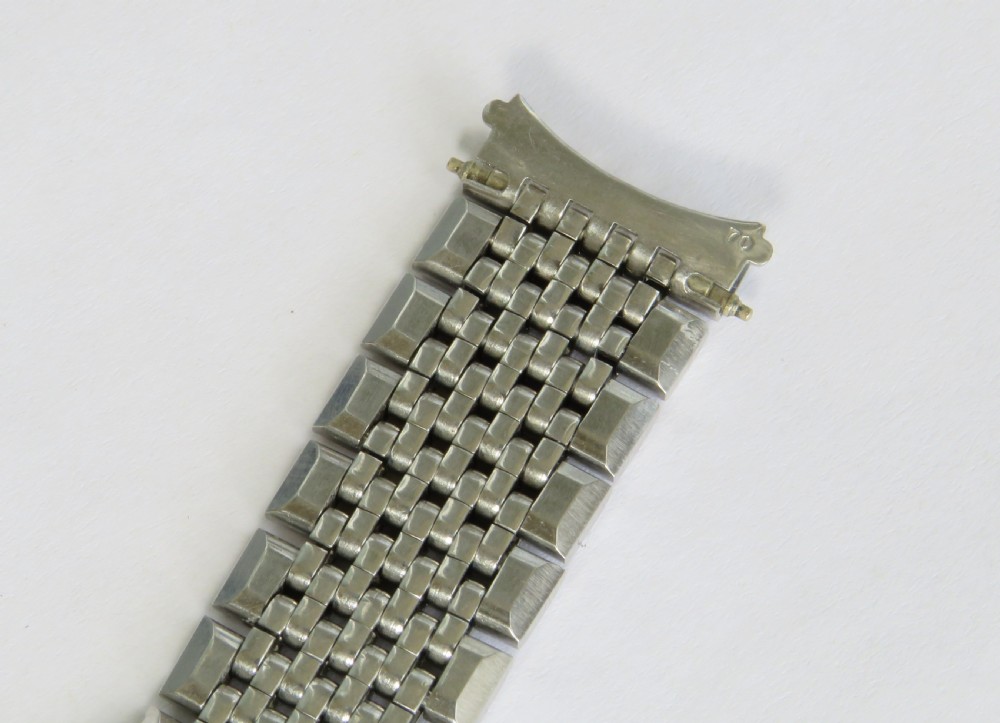 An overhead view of a segmented stainless steel Omega watch bracelet with a branded clasp against a neutral background. View IV