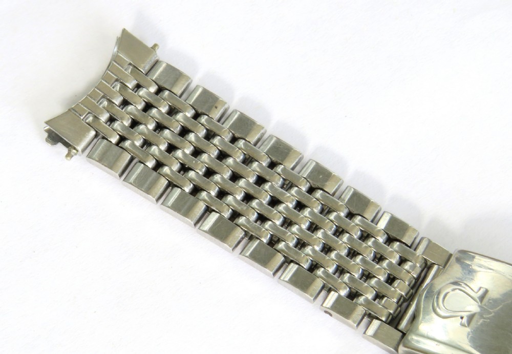 An overhead view of a segmented stainless steel Omega watch bracelet with a branded clasp against a neutral background. View VI