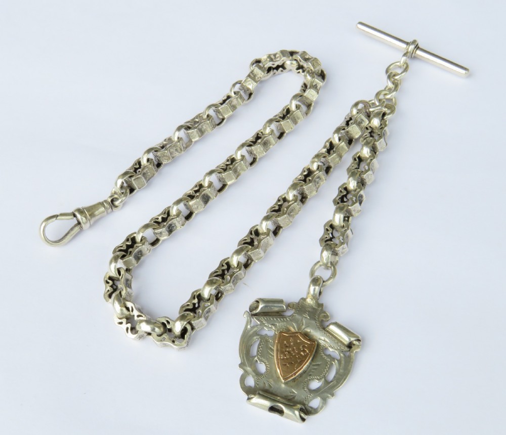 An antique sterling silver Albert watch chain featuring patterned fancy links, a T-bar fastener, a swivel clip, and a shield-shaped fob with a gold cartouche.