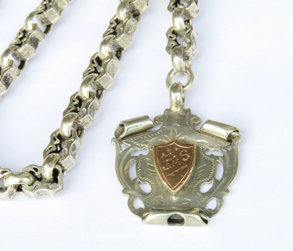 An antique sterling silver Albert watch chain featuring patterned fancy links, a T-bar fastener, a swivel clip, and a shield-shaped fob with a gold cartouche. View II